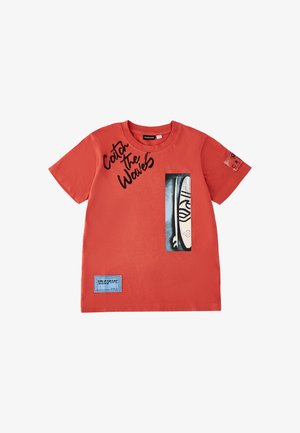 Maglietta rossa a maniche corte con la scritta "Catch the Waves", una grafica di tavola da surf e toppe cucite blu e rosse sul davanti e sulla manica.