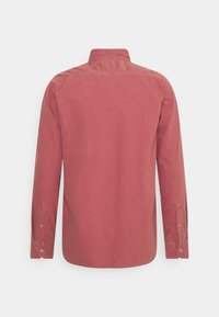 Chemise à manches longues en coton rose poussiéreux, poignets boutonnés et col classique. Texture lisse avec un détail de couture discret.