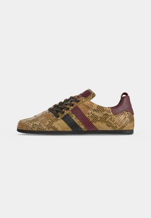 Niedriger Sneaker mit braunem Schlangenledermuster, schwarzen und dunkelroten Streifen, schwarzen Schnürsenkeln und dunkelrotem Fersenlasche auf flacher schwarzer Sohle.