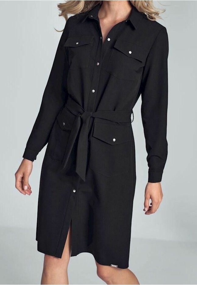 Femme portant une robe noire à manches longues boutonnée à l’avant, avec des poches devant et une ceinture nouée à la taille, devant un fond gris uni.