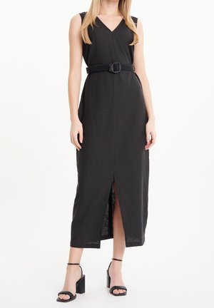Donna che indossa un vestito midi nero senza maniche con spacco frontale, vita con cintura e sandali neri con tacco a blocco e cinturino alla caviglia.
