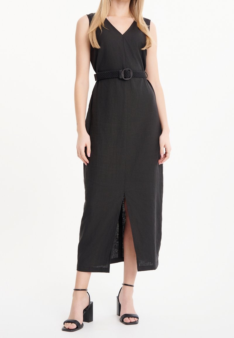 Femme portant une robe midi noire sans manches avec une fente à l’avant, une taille ceinturée et des sandales à talons blocs noires avec bride à la cheville.