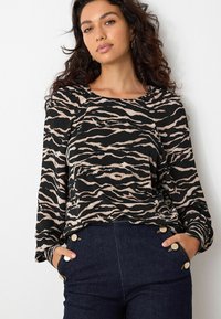 Top de manga larga en negro con rayas de cebra beige, con un cuello redondo y textura suave. Combinado con pantalones de mezclilla oscuros con botones dorados.