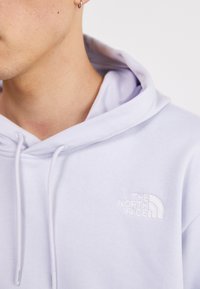 Felpa leggera viola chiaro realizzata in materiale misto cotone. Presenta un cappuccio con coulisse e un logo ricamato sul petto. Tessuto morbido.