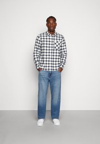 Camicia a quadri blu navy e bianca con taschino sul petto, abbinata a jeans a gamba dritta blu chiaro e sneakers bianche. Design semplice.