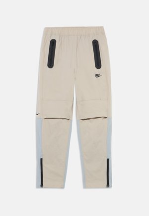 Beige athletic pants with black zippered pockets, elastic waistband, and light blue accents on the sides. Features zippers at the ankles.