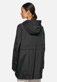 Zwarte waterdichte jas met een capuchon. Kenmerkt zich door een losse pasvorm, schoudernaden en een gladde, glanzende textuur. Geen zichtbare sluitingen.