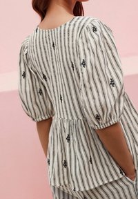 Blouse à rayures blanches et noires avec des manches courtes bouffantes, design peplum, détails de broderie florale et col rond.