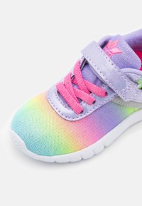 Színes sneaker, hálós felső résszel, amely a rózsaszínről zöldre halad, rózsaszín fűzőkkel és tépőzáras pánttal kiemelve. Fehér talp.