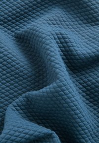 Tessuto texturizzato di colore blu profondo, con un motivo a diamante trapuntato e bordi morbidi e ondulati. Textura intrecciata visibile.