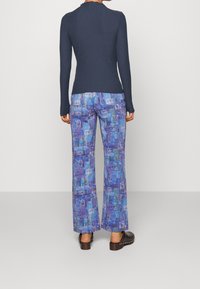 Haut à manches longues côtelé bleu marine associé à un pantalon à jambes larges présentant un patchwork coloré de tons bleus et de motifs graphiques. Des sabots marron sont portés.