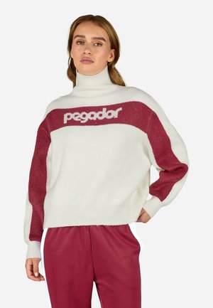 Cream-colored sweater with a high collar, featuring maroon accents and a logo across the chest. Made of soft, textured material.