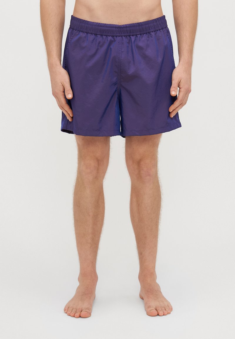 Costumi da bagno viola realizzati in tessuto leggero con vita elastica e tasche laterali, progettati per il comfort e la facilità di movimento.