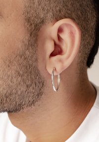 Boucle d'oreille en argent portée sur un oreille en gros plan avec des cheveux courts, mettant en valeur une finition polie et un design circulaire.