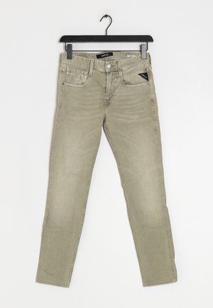 Jean slim beige avec poches avant et poche monnaie, passants de ceinture, fermeture par bouton, suspendu à un cintre en plastique noir sur fond blanc.