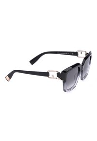 Lunettes de soleil carrées noires surdimensionnées avec verres teintés en dégradé et accents d'articulations argentés sur fond blanc.