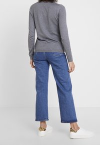 Grå langærmet trøje, blå denim jeans og hvide sneakers med leopardprint-detaljer på hælen, set fra ryggen.
