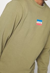 Olivově zelená mikina z bavlněné směsi s malým modro-růžovým logem Levi's na přední straně. Klasický kruhový výstřih.