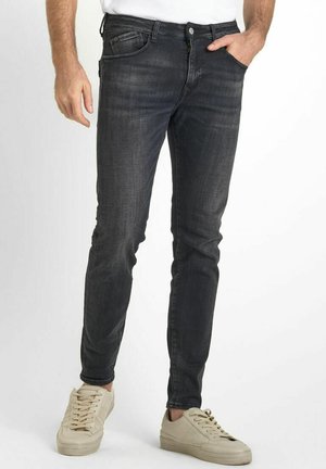 Slim-fit, dark gray denim jeans with a subtle texture, five pockets, and metal button closure, paired with light beige sneakers.