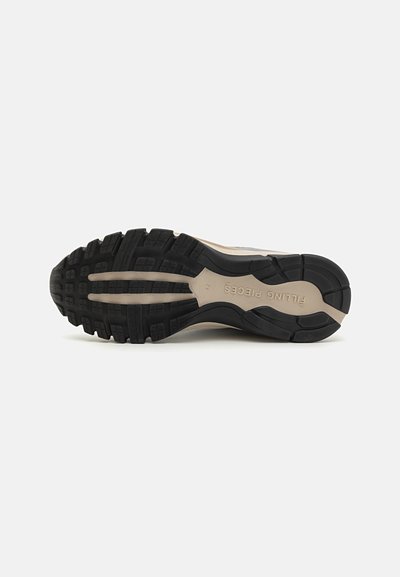 Semelle en caoutchouc noir avec des motifs de semelle profonds, dotée d'un intersemelle beige et d'un texte de marque. Conçue pour l'adhérence et la durabilité.