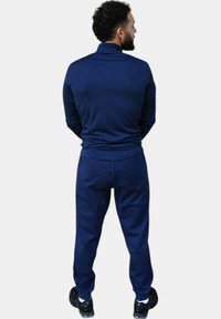 Chándal deportivo azul marino hecho de tela suave; parte superior ajustada de manga larga con cuello alto; pantalones cónicos a juego; zapatillas negras.