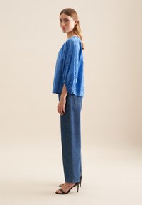 Blå bomuldsbluse med blomsterbroderi, afslappet pasform og pufærmer. Sammen med højtaljede, lige ben denim jeans og hæle.