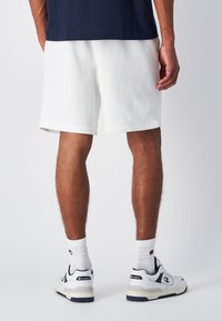 Pantalones cortos de algodón blancos con un corte relajado, con un dobladillo acanalado. Combinados con calcetines blancos y zapatillas deportivas en blanco, con detalles en azul marino y gris.