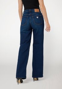 Mörkblå vida jeans med hög midja, femficksdesign och en brun läderlapp vid bakmidjan med en logotyp.