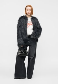 Μαύρο τζάκετ από ψεύτικη γούνα, λευκό μπλουζάκι με γραφικά, σκούρο τζιν με φαρδιά μπατζάκια και μικρή μαύρη τσάντα με ασημένιες λεπτομέρειες. Σχεδιασμός με υφή και πολλαπλές στρώσεις.