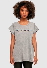 Pilkas didelis marškinėliai su apvaliu kaklu ir trumpomis sukritusiomis rankovėmis. Priekyje yra daugiaspalvis „IRON MAIDEN“ tekstas. Minkšta tekstūra.