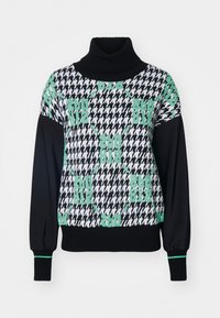 Mustat ja valkoiset houndstooth-kuvioidut villapaidat, joissa on korkea kaulus, kirkkaan vihreät yksityiskohdat ja ribbikuvioiset hihansuut. Materiaalit näyttävät pehmeiltä ja neulotuilla.