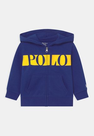 Sudadera con cremallera en color navy, hecha de algodón, que presenta un gran gráfico amarillo de "POLO" en el pecho, bolsillos tipo canguro y capucha.