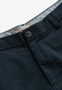 Navyblaue Baumwollhosen mit einem frontalen Knopfverschluss, Gürtelschlaufen und einem gemusterten Innenbund. Glatte Textur ohne sichtbare Muster.