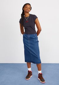 Black short-sleeve T-shirt with red "OBEY" text, paired with a blue denim midi skirt and brown sneakers with pink accents.