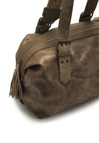 Sac à main en cuir artificiel brun avec des accents texturés, fermeture éclair, détails en franges et bandoulière réglable. Forme ronde et finition douce.