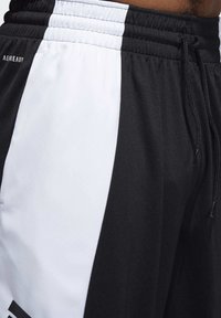 Schwarz-weiße Sportshorts mit einem dehnbaren Bund, Kordelzug und Seitenpanele-Design. Das Material wirkt glatt und leicht.