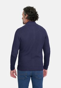 Suéter de punto en color navy con cuello alto, puños y dobladillo acanalados; presenta una tela texturizada y un ajuste relajado, combinado con jeans azules.