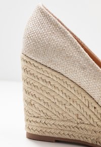 Béžové espadrilové sandály na platformě s tkaným textilním svrškem, spleteným juteovým podpatkem a hladkou hnědou podrážkou. Design zahrnuje špičatou špičku.