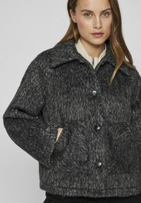 Pelēka teksturēta vilnas jaka ar apkakli, ar divām priekšējām kabatām, pogu aizdari un brīvu piegriezumu.