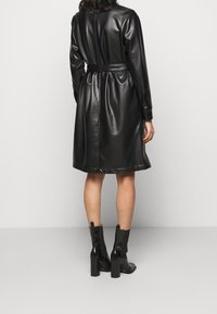 Černé šaty z umělé kůže s páskem v oblasti pasu, navržené s polodlouhým střihem a dlouhými rukávy. Hladká textura, jednoduchý a elegantní design.