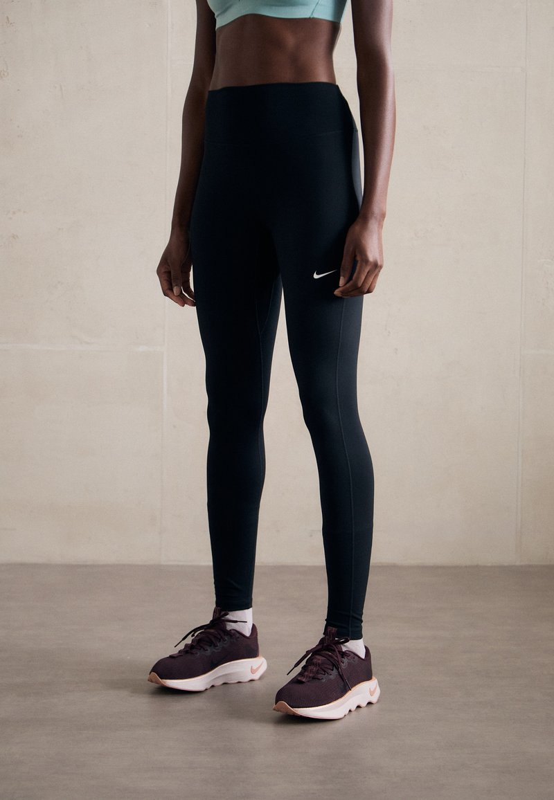 Black high-waisted leggings with a sleek fit and Nike logo, paired with dark purple athletic shoes featuring a white sole and accents.