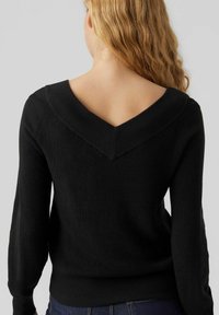 Pullover nero in maglia con un profondo design a V sulla schiena, polsini e orlo a costine. Il materiale testurizzato presenta una finitura liscia e uno stile a maglia fitta.