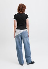 Black fitted t-shirt with white trim at sleeves, paired with loose blue denim jeans. A white knitted accessory drapes around the waist.