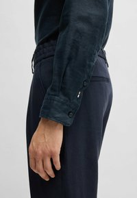 Granatowa koszula z guzikami, o teksturowanym wykończeniu i podwiniętych mankietach, zestawiona z ciemnymi spodniami z regulowanym pasem.