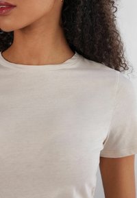 T-shirt corto a maniche corte color beige chiaro con scollo rotondo, in morbido cotone e cuciture piatte, caratterizzato da una superficie liscia e una vestibilità standard.