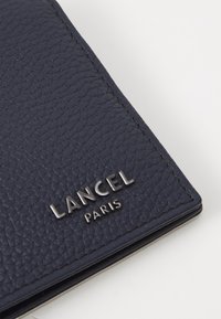 Granatowy portfel skórzany o teksturowanym wykończeniu, z logo LANCEL PARIS w kolorze srebrnym w dolnym prawym rogu.