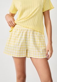 Top amarilla de manga corta con textura acanalada, combinado con pantalones cortos a rayas amarillas y blancas que cuentan con una cinturilla elástica y un borde de encaje.