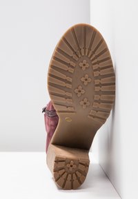 Semelle d'une botte cheville bordeaux avec un talon en bois épais, montrant un motif détaillé de la bande de roulement et une étiquette de taille 37 sur une surface blanche.