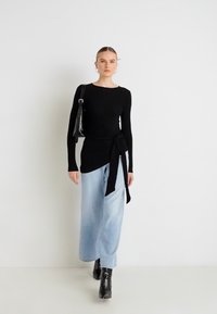 Bluză neagră cu mâneci lungi și detaliu cu fundă la talie, asortată cu blugi largi bleu deschis și ghete negre până la gleznă. Estetică minimalistă.