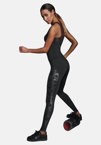 Kobieta w czarnym stroju sportowym używa wałka piankowego pod prawą stopą, z lewą ręką zgiętą i lewą nogą wyciągniętą do tyłu.